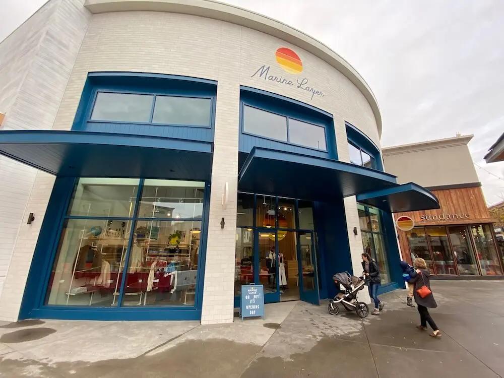 Marine Layer storefront with blue trim and large windows, with pedestrians and a stroller outside.