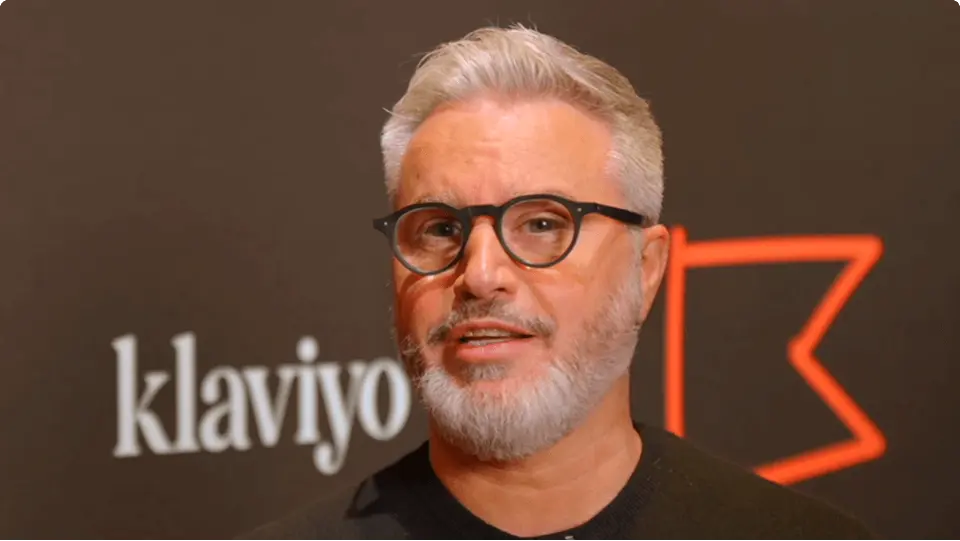 A man with glasses and a beard speaks in front of a backdrop featuring the Klaviyo logo.