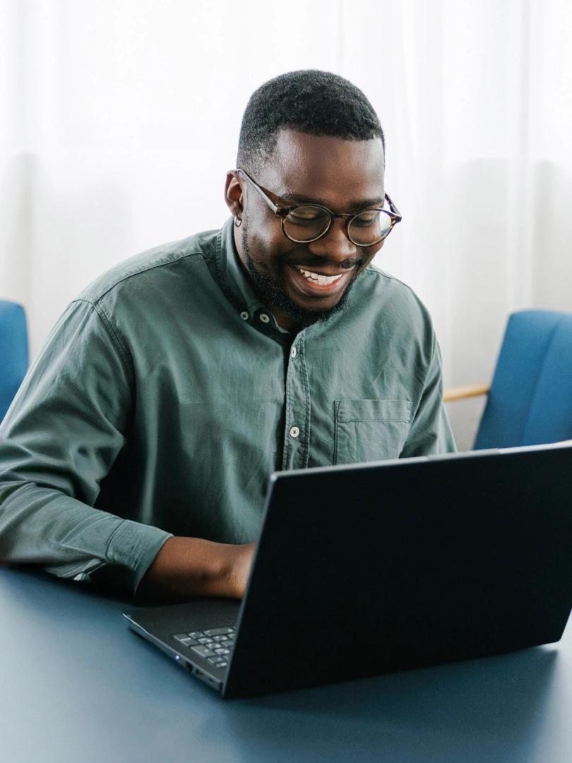 Smiling man wearing glasses works on a laptop at a table.