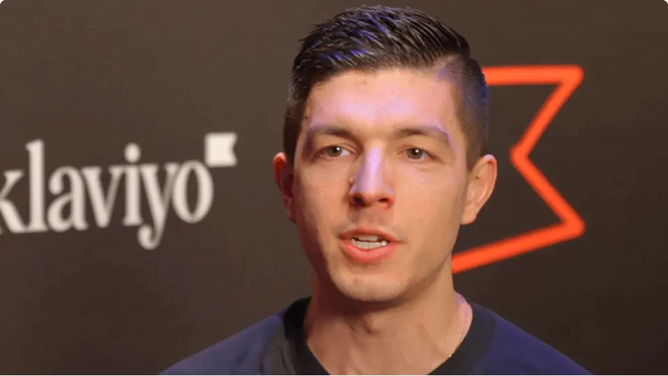 A person speaking in front of a backdrop with the Klaviyo logo.