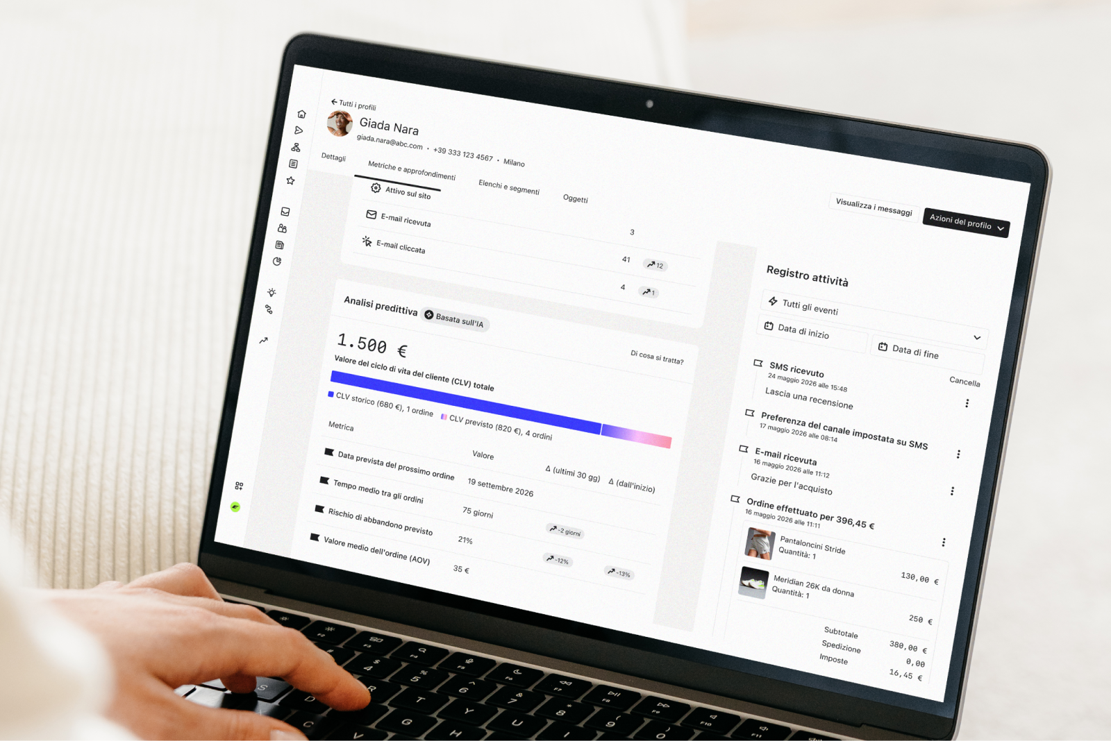 Una persona usa un laptop che mostra un profilo cliente, l'analisi predittiva e il registro delle attività.