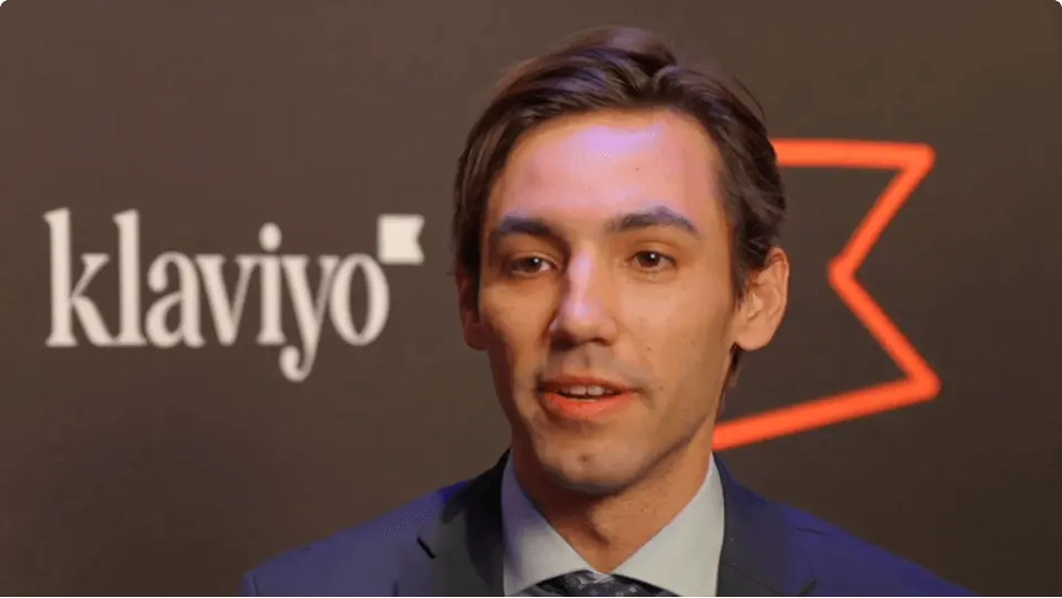 A person speaking in front of a backdrop featuring the Klaviyo logo.