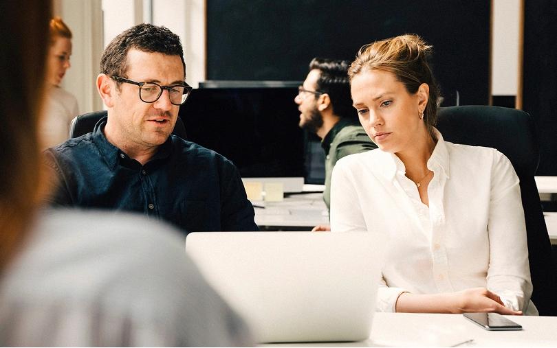 Man talking to a woman as they look at a laptop in an office.