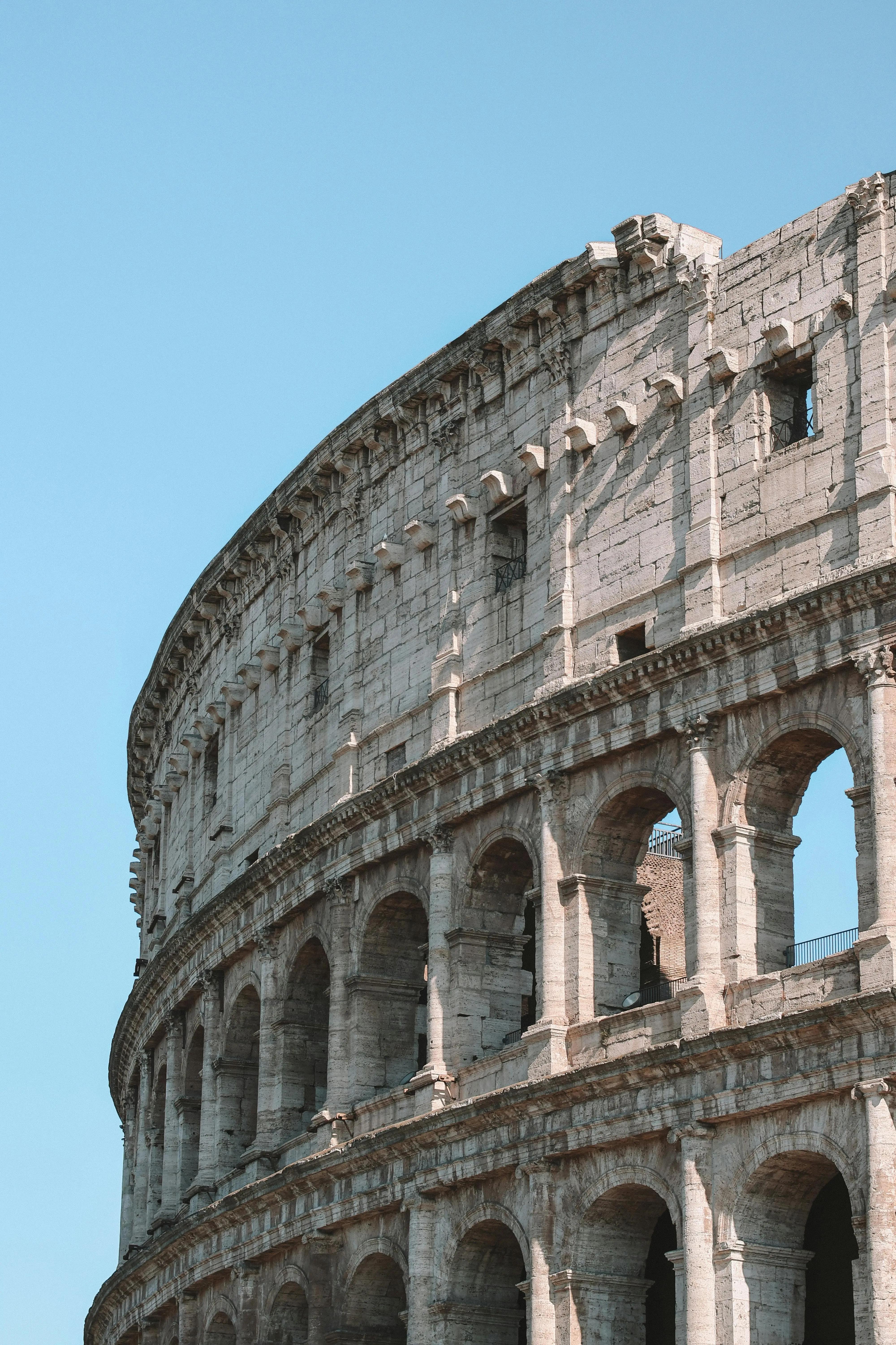 Gros plan sur la façade du Colisée à Rome, mettant en valeur ses arches et sa structure en pierre ancienne sous un ciel bleu clair.