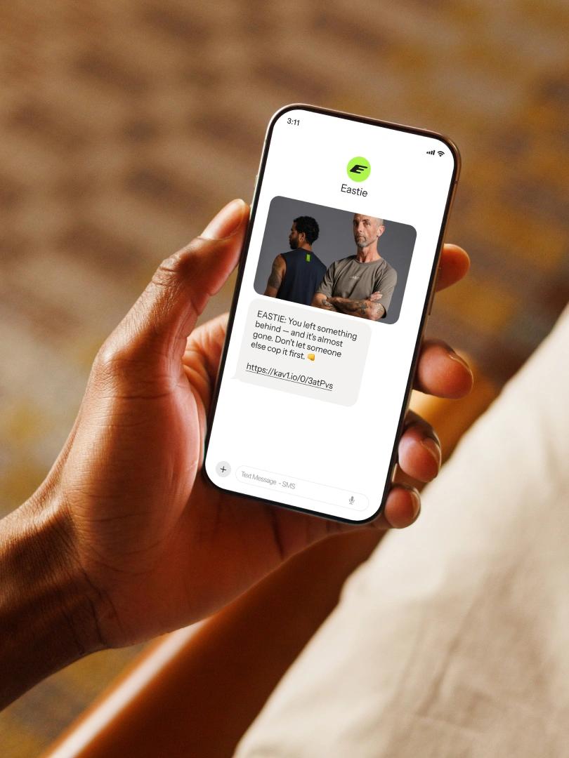 Person holding a smartphone displaying an Eastie reminder text with a clothing product photo and link.