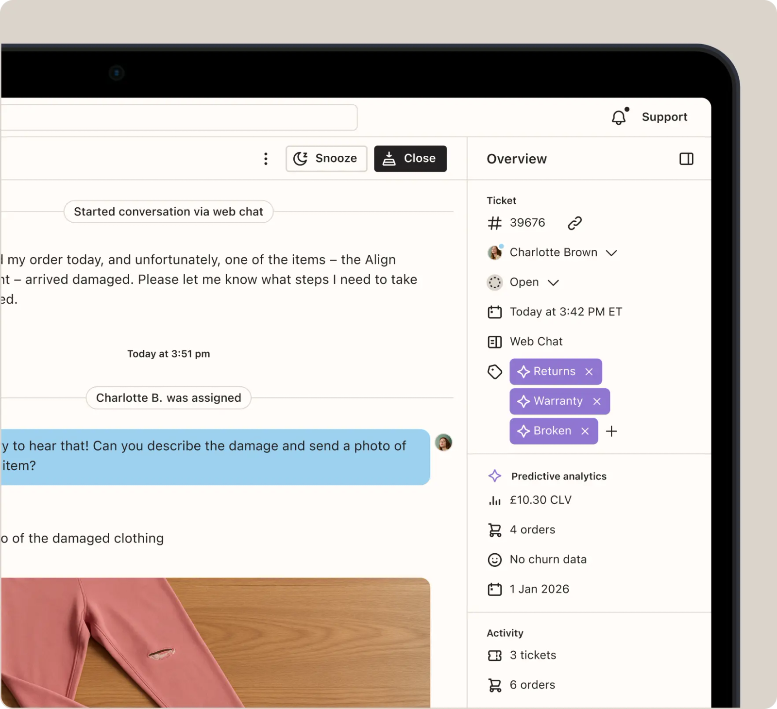 Image shows a helpdesk ticket on a tablet, split into a conversation on the left and an “Overview” sidebar on the right. The shopper’s message, partly cut off by the crop, reports that an item arrived damaged. The agent, Charlotte B., asks them to describe the damage and send a photo, followed by a photo of pink leggings with a tear. The sidebar shows the ticket tagged “Returns,” “Warranty,” and “Broken.”