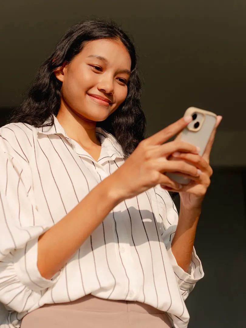 Smiling young woman using a smartphone in warm sunlight.