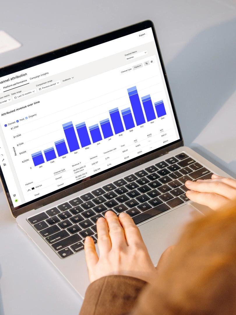 Person using a laptop displaying a channel attribution dashboard with monthly revenue bar charts.