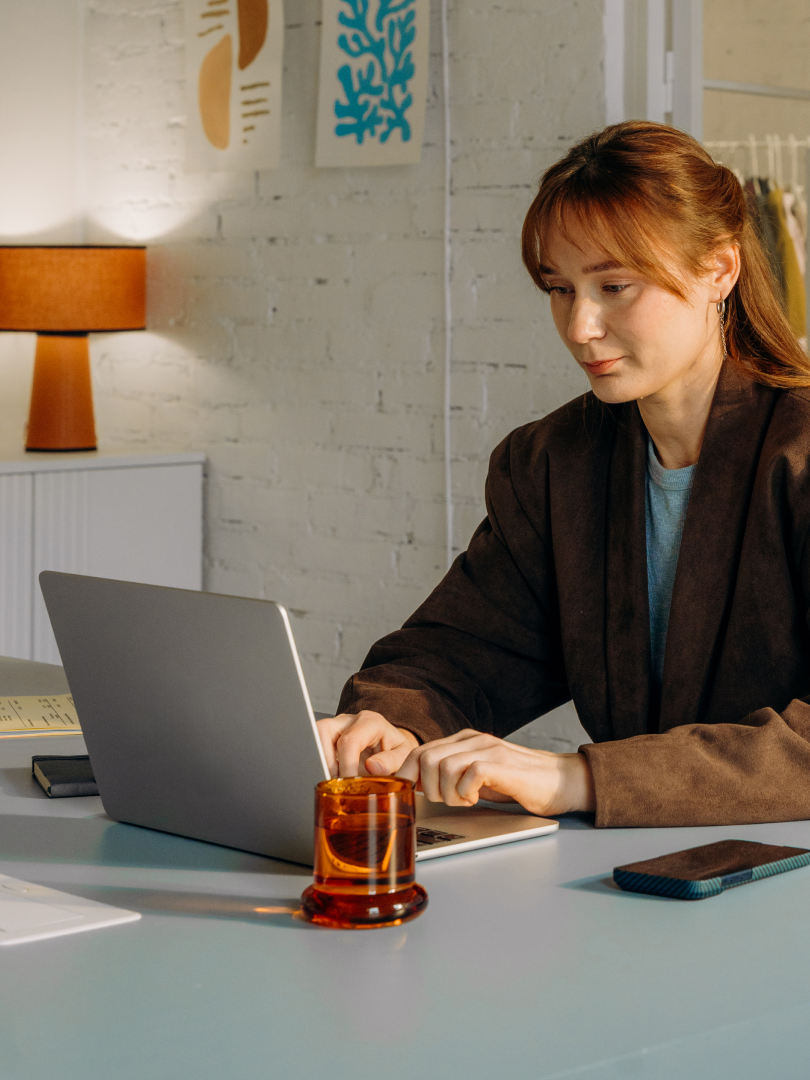 Woman working on a laptop at a desk in a warmly lit office