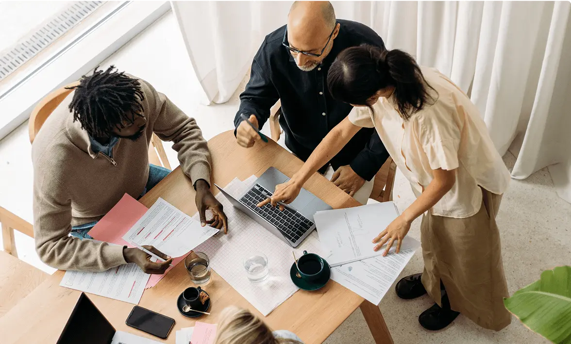 People collaborating around a table with documents and a laptop.