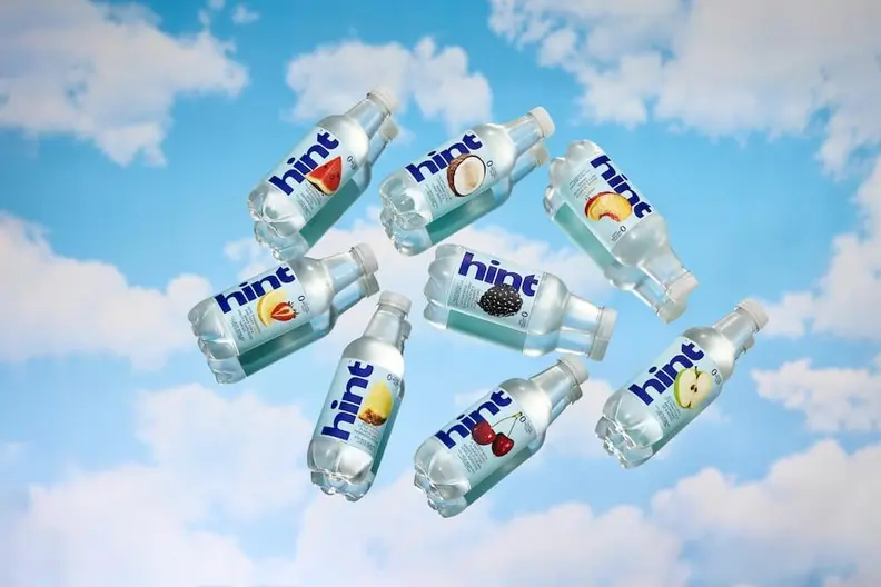 Eight Hint flavored water bottles in various fruit flavors floating against a blue sky with white clouds.