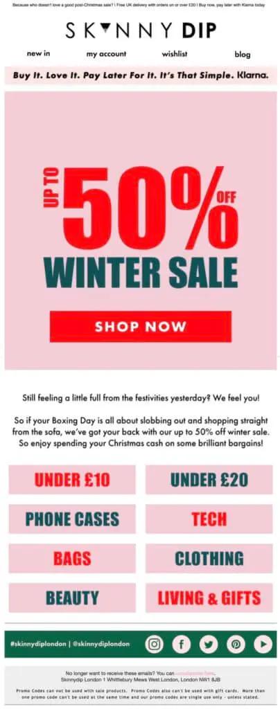 Image shows a Boxing Day marketing email from lifestyle fashion brand Skinnydip London, featuring bright red and blue font on a millennial pink background that reads, “up to 50% off winter sale.” The prominent CTA button reads, “shop now.”