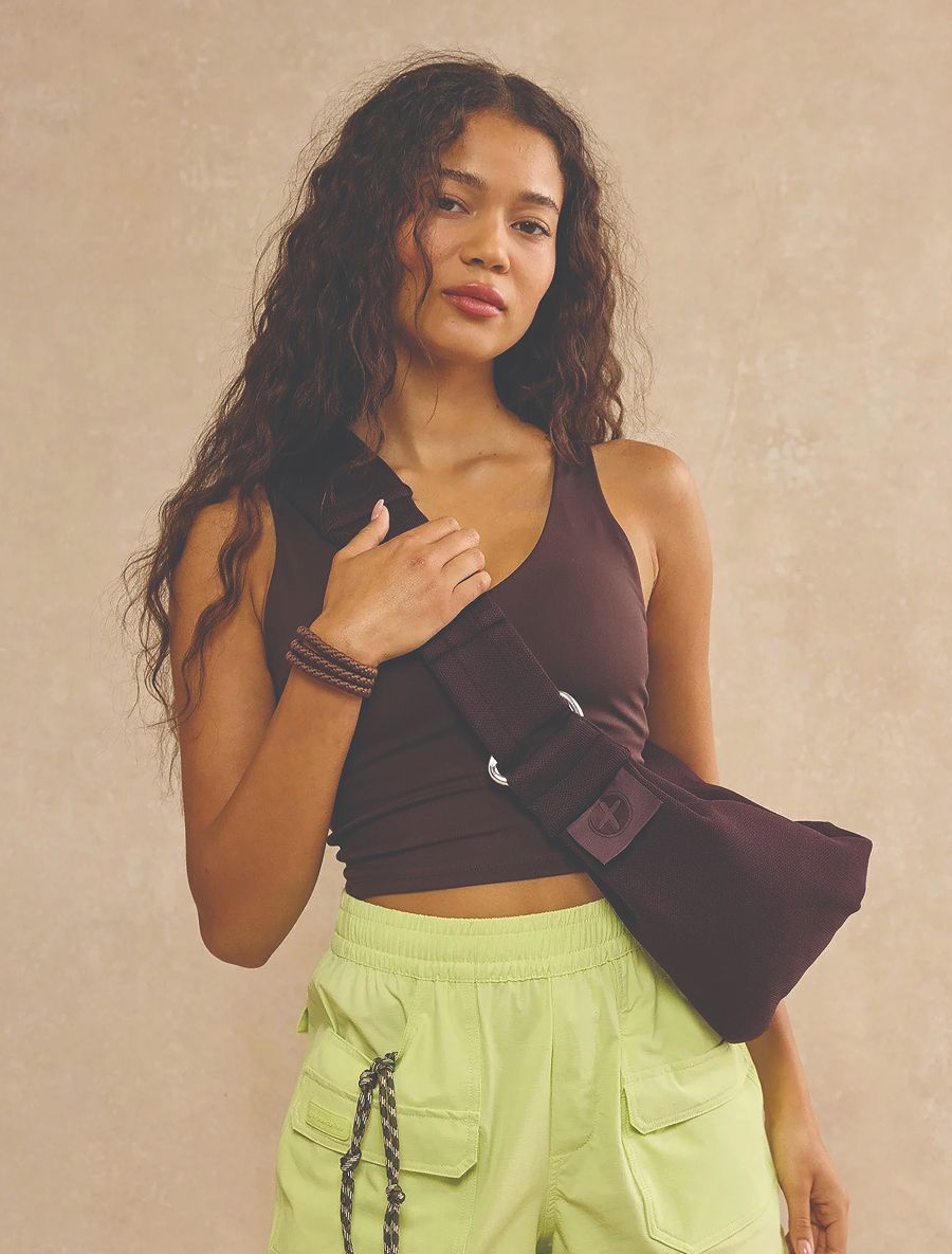A young woman wears a dark brown tank top and sling bag with lime green cargo shorts.
