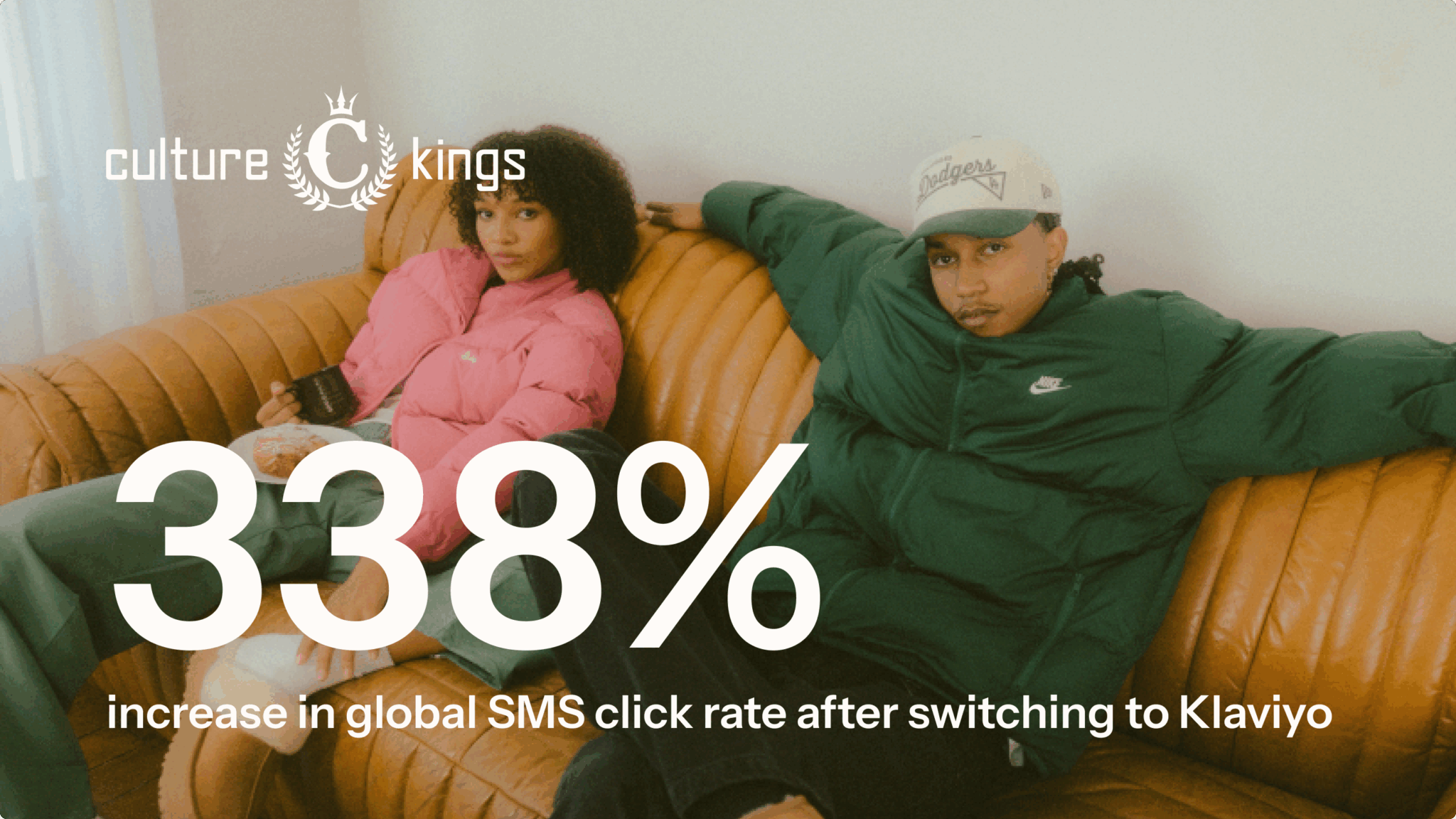 Two people sitting on a couch, one in a pink jacket and the other in a green jacket and cap. Text: "338% increase in global SMS click rate after switching to Klaviyo." Culture Kings logo.