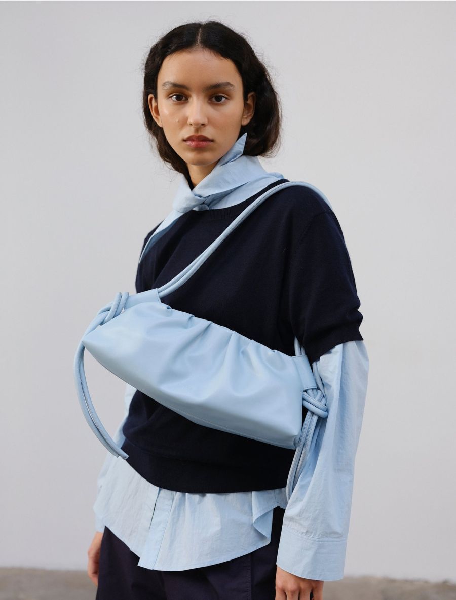 Una mujer con un jersey azul marino sobre una camisa azul claro y un bolso bandolera a juego.