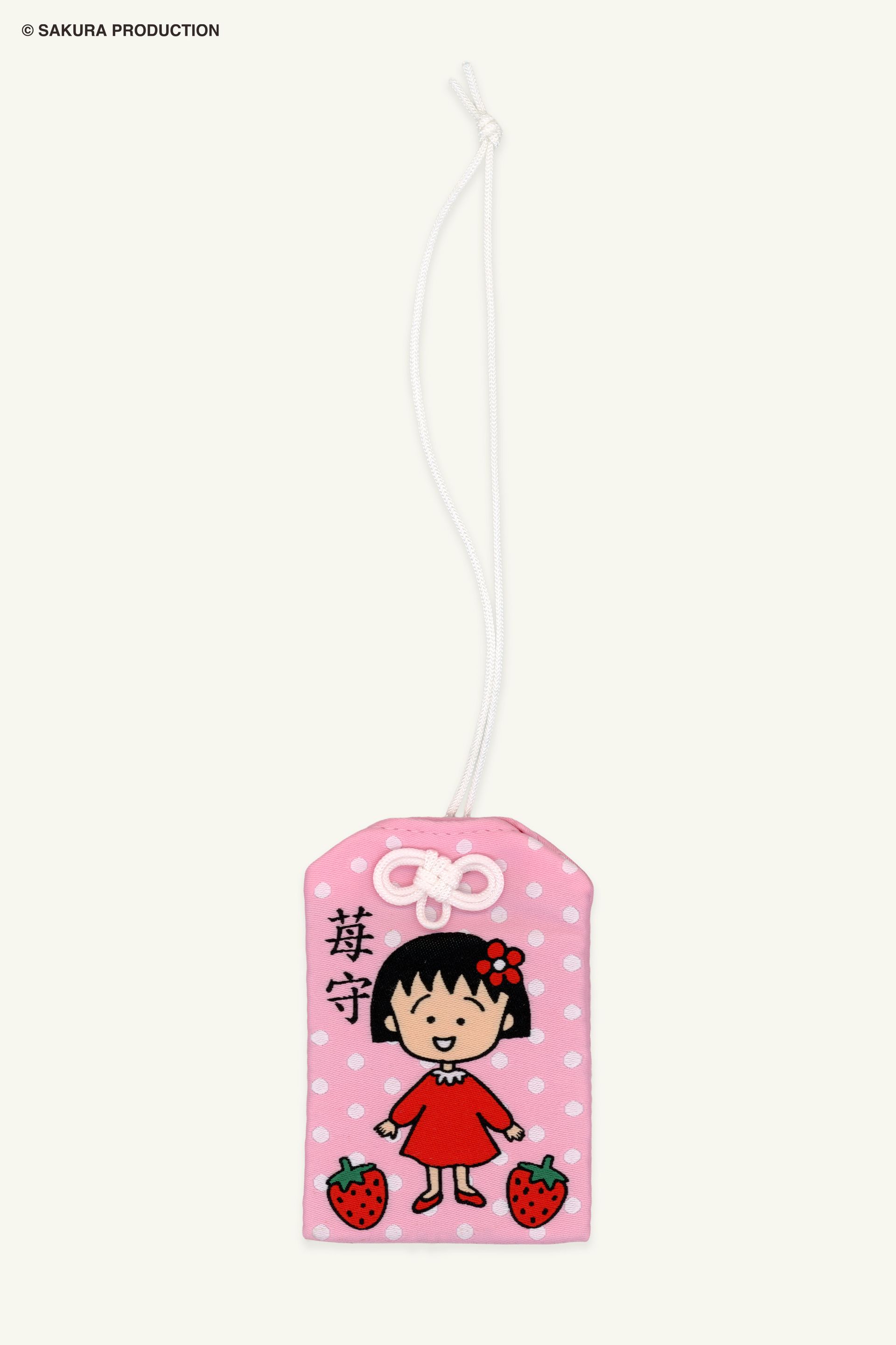 Flat image of Chibi Maruko Chan Omamori Keychain. Pink omamori charm with white polka dots, Chibi Maruko-chan in a red dress, and two strawberries. In Japanese in reads "Strawberry Protection." 