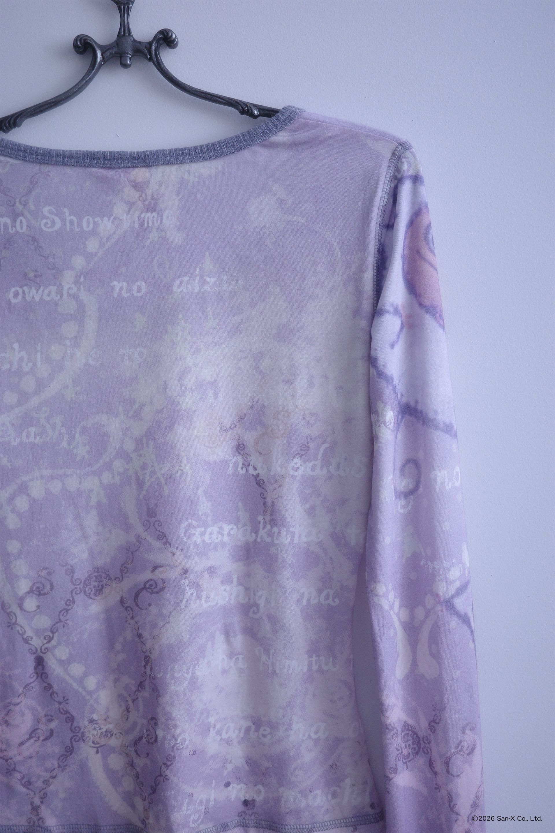 Close up flat image of a hanger holding an ethereal engineered print long-sleeve top featuring Shappo the Ringmaster. Cut from a lightweight, 110gsm 100% Cotton with chunky, heathered dusty purple ribbing at the neck and sleeve cuffs. The sleeves are finished with taller cuffs and built-in thumb holes, providing extra coverage and keeping your hands warm during the colder months.