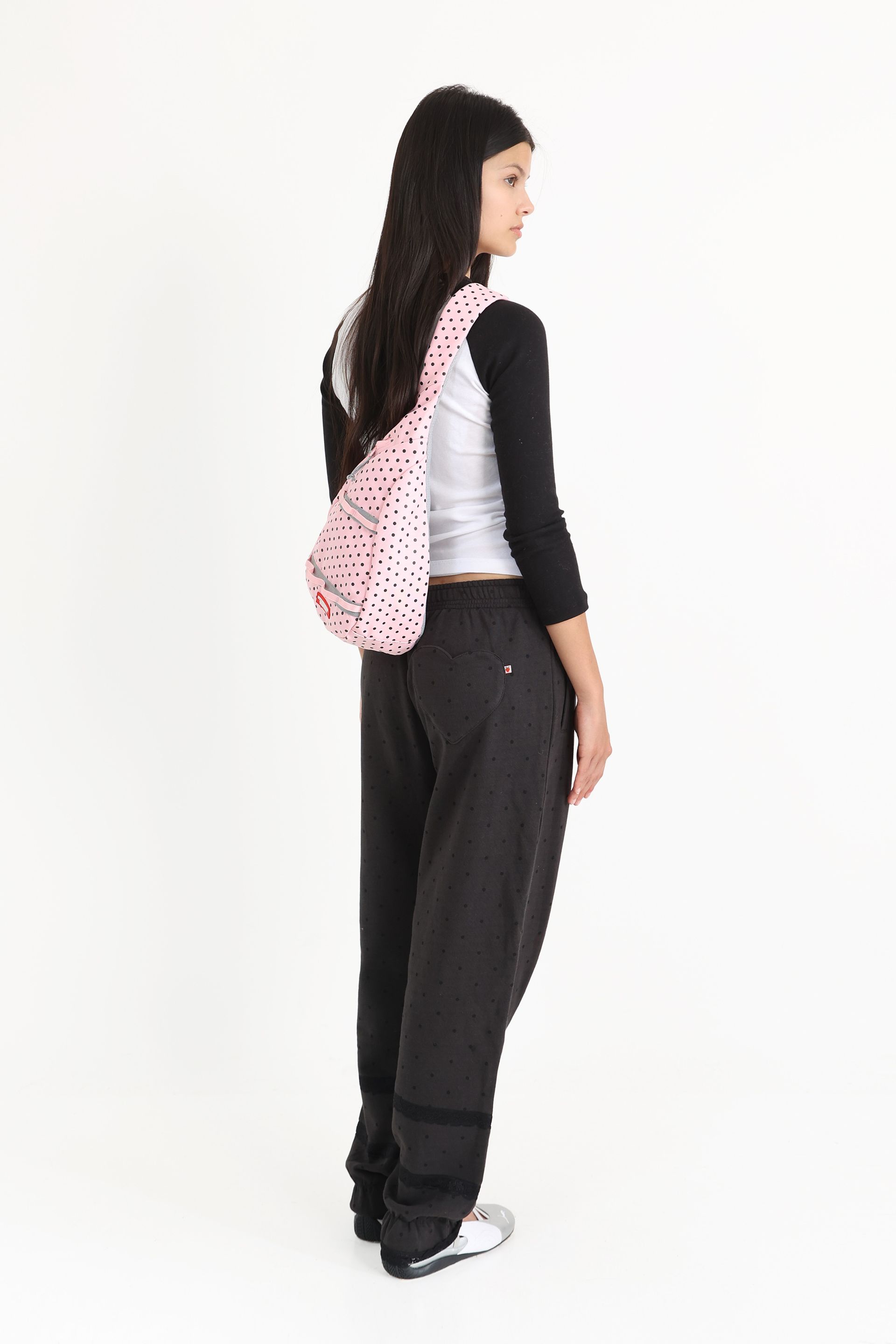 Model carries a pink polka-dotted sling bag over one shoulder, which rests against her back.