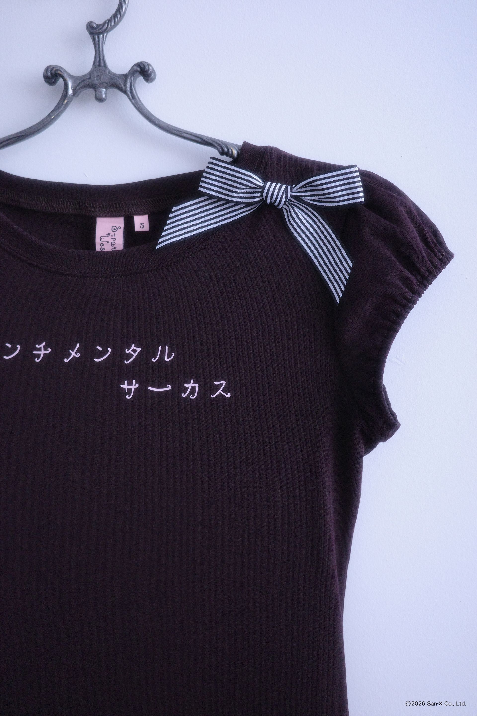 Close up flat image of front of the Sweets top. Short sleeve, brown, ruffle hem top with Japanese that reads "Sentimental Circus" across the chest. Black and white stripe bow on shoulder.