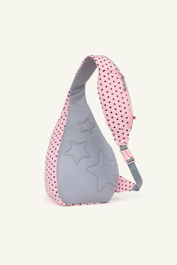 Back view of a pink sling backpack with black polka dots and a gray padded panel featuring embossed star shapes. The bag has a gray adjustable strap with a pink buckle and a small zip pocket on the strap.