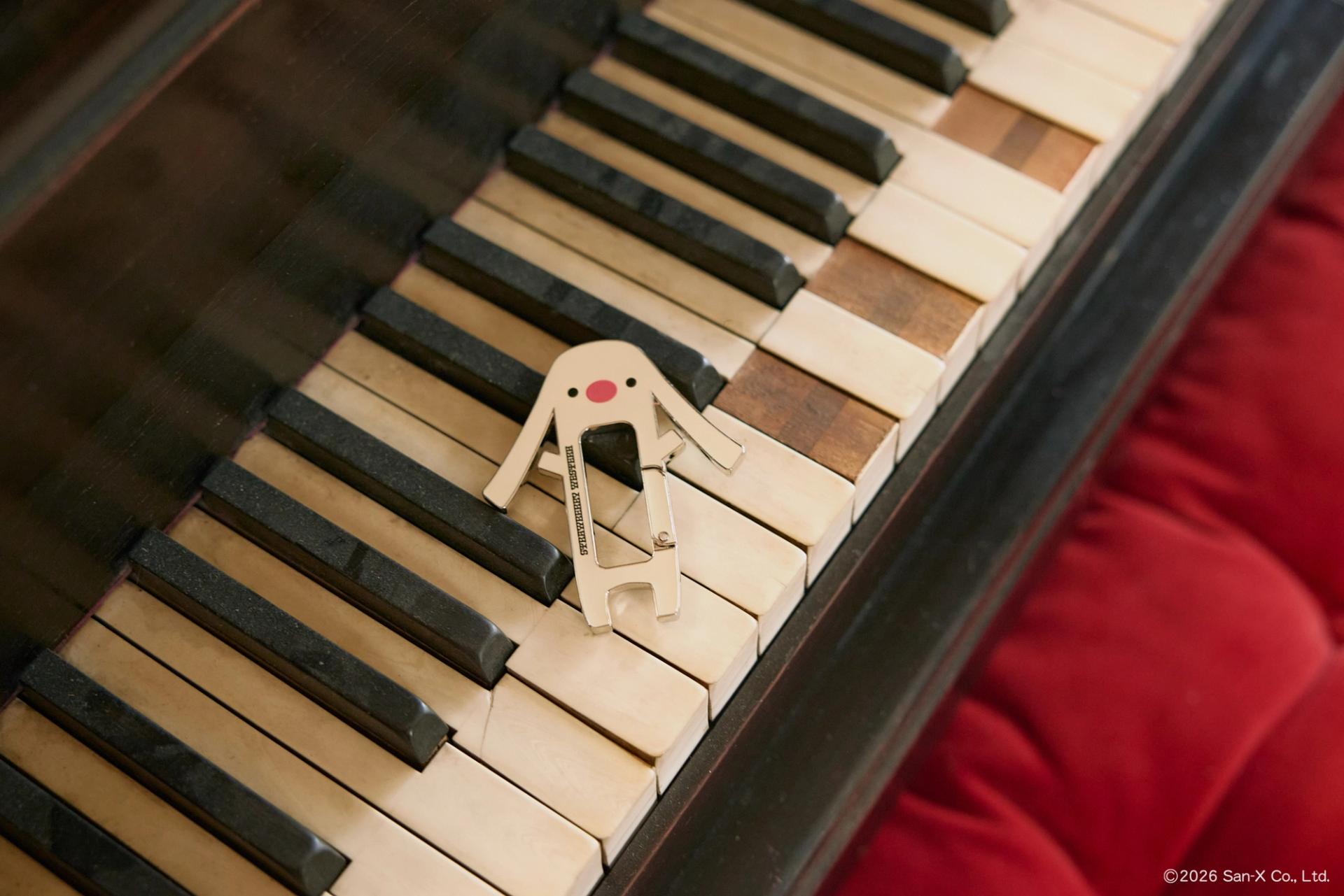 Toto, a character from Sentimental Circus, Carabiner Keychain laid out on the broken keys of a grand piano.