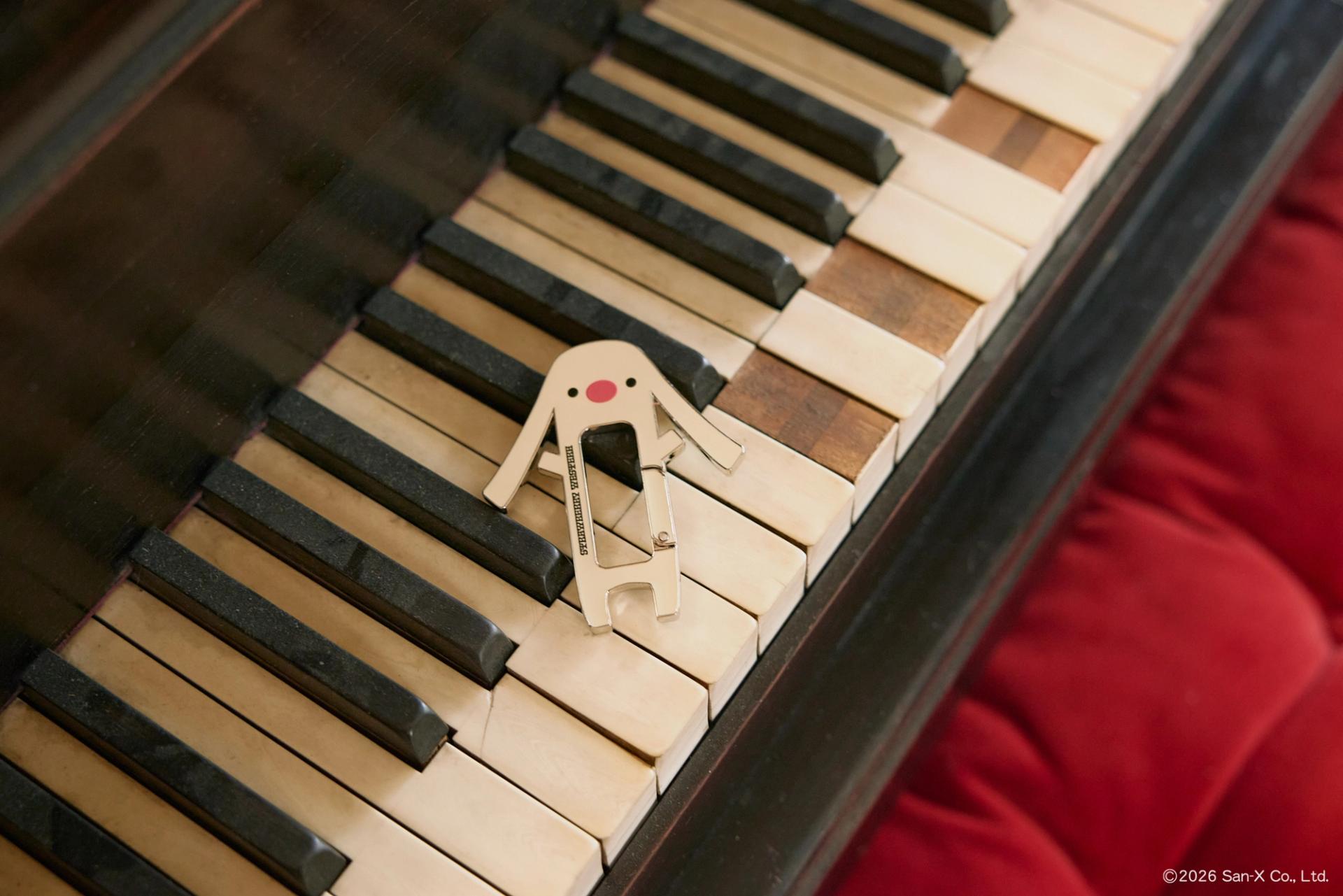 Toto, a character from Sentimental Circus, Carabiner Keychain laid out on the broken keys of a grand piano.