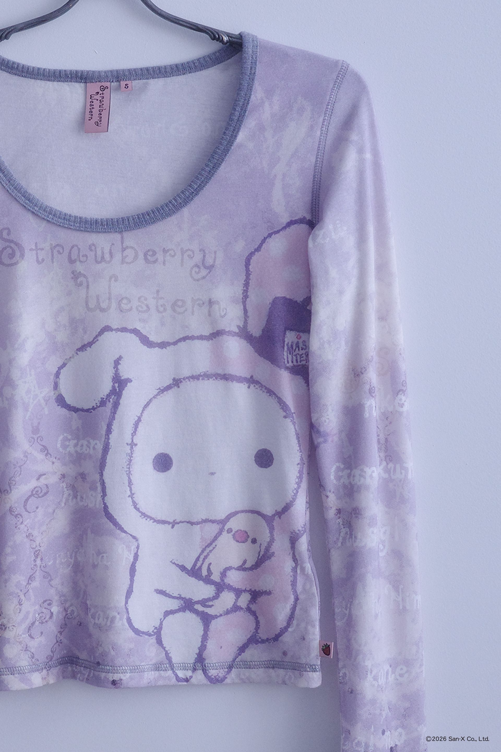 Close up flat image of a hanger holding An ethereal engineered print long-sleeve top featuring Shappo the Ringmaster. Cut from a lightweight, 110gsm 100% Cotton with chunky, heathered dusty purple ribbing at the neck and sleeve cuffs. The sleeves are finished with taller cuffs and built-in thumb holes, providing extra coverage and keeping your hands warm during the colder months.