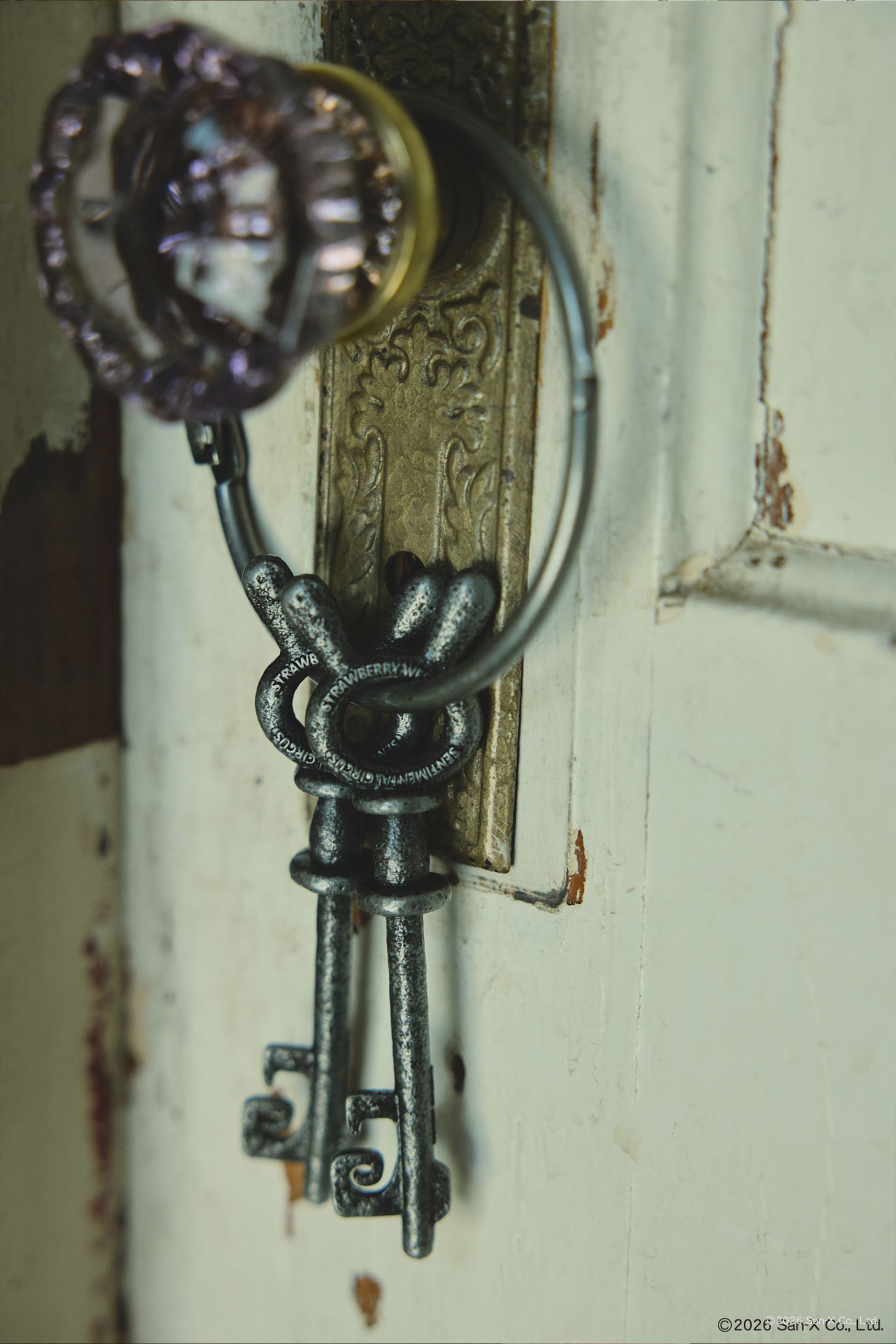 Close up image of a victiorian door knob holding a pair of two beautiful and heavy Sentimental Circus skeleton keys on a large hinged, jailer ring. These bunny head keys were brought to life from 2D in a cast iron texture featuring the Sentimental Circus and Strawberry Western logos on both sides. 