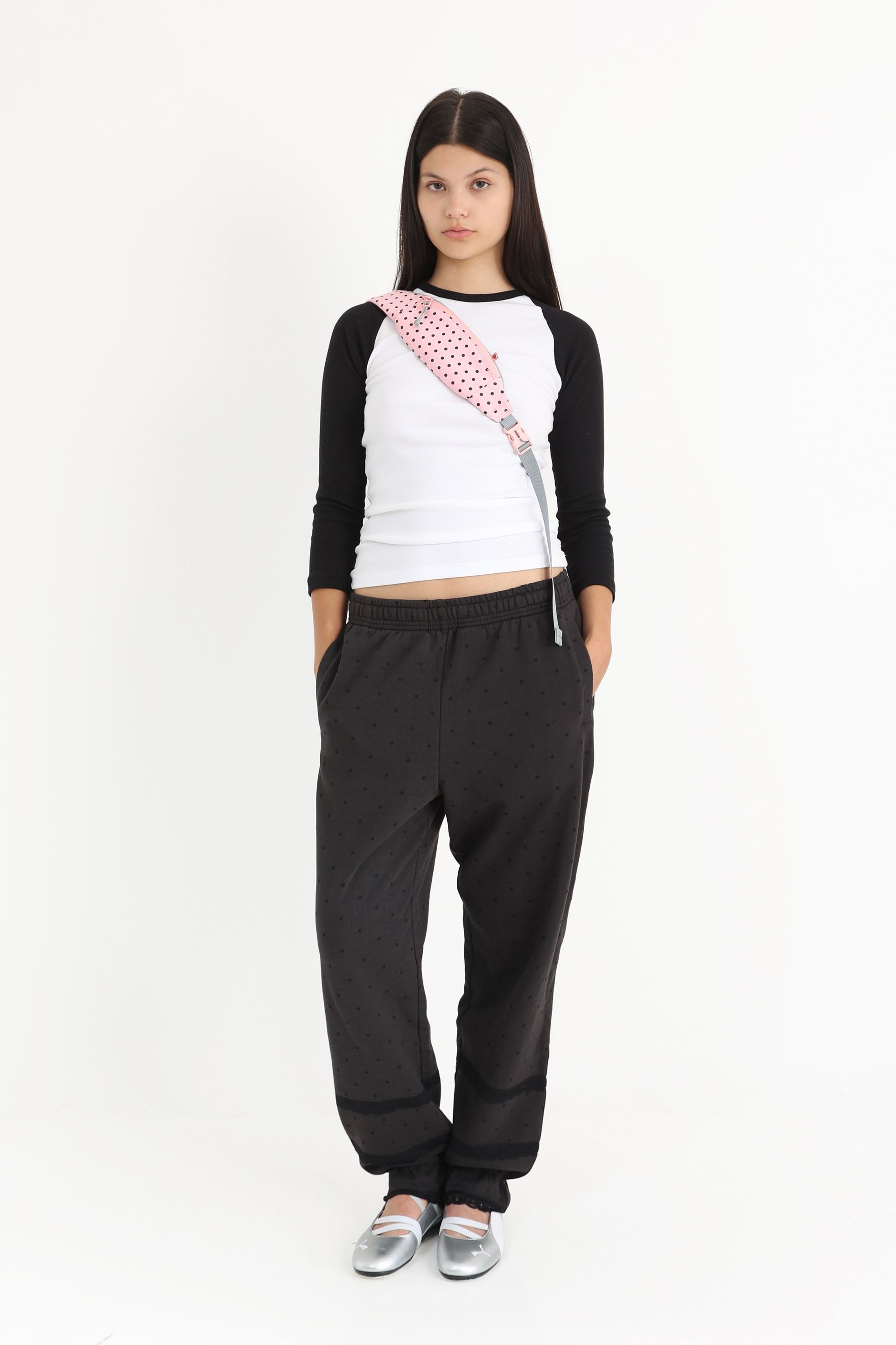 Model has a pink crossbody bag with black polka dots slung across her chest and her hands in her pockets, giving a relaxed and casual look.