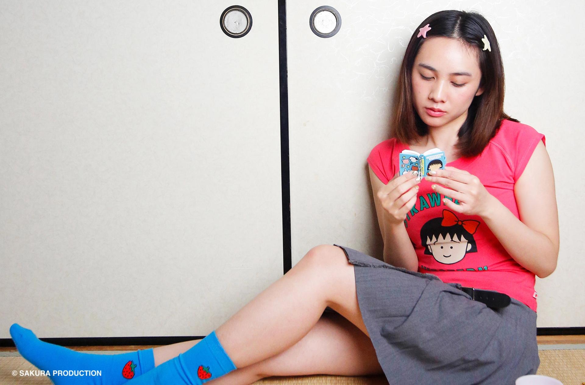Girl sitting wearing Chibi Maruko Chan Raglan top in Hot pink, wearing blue socks, and reading from the Chibi Maruko Chan Secret Notebook.