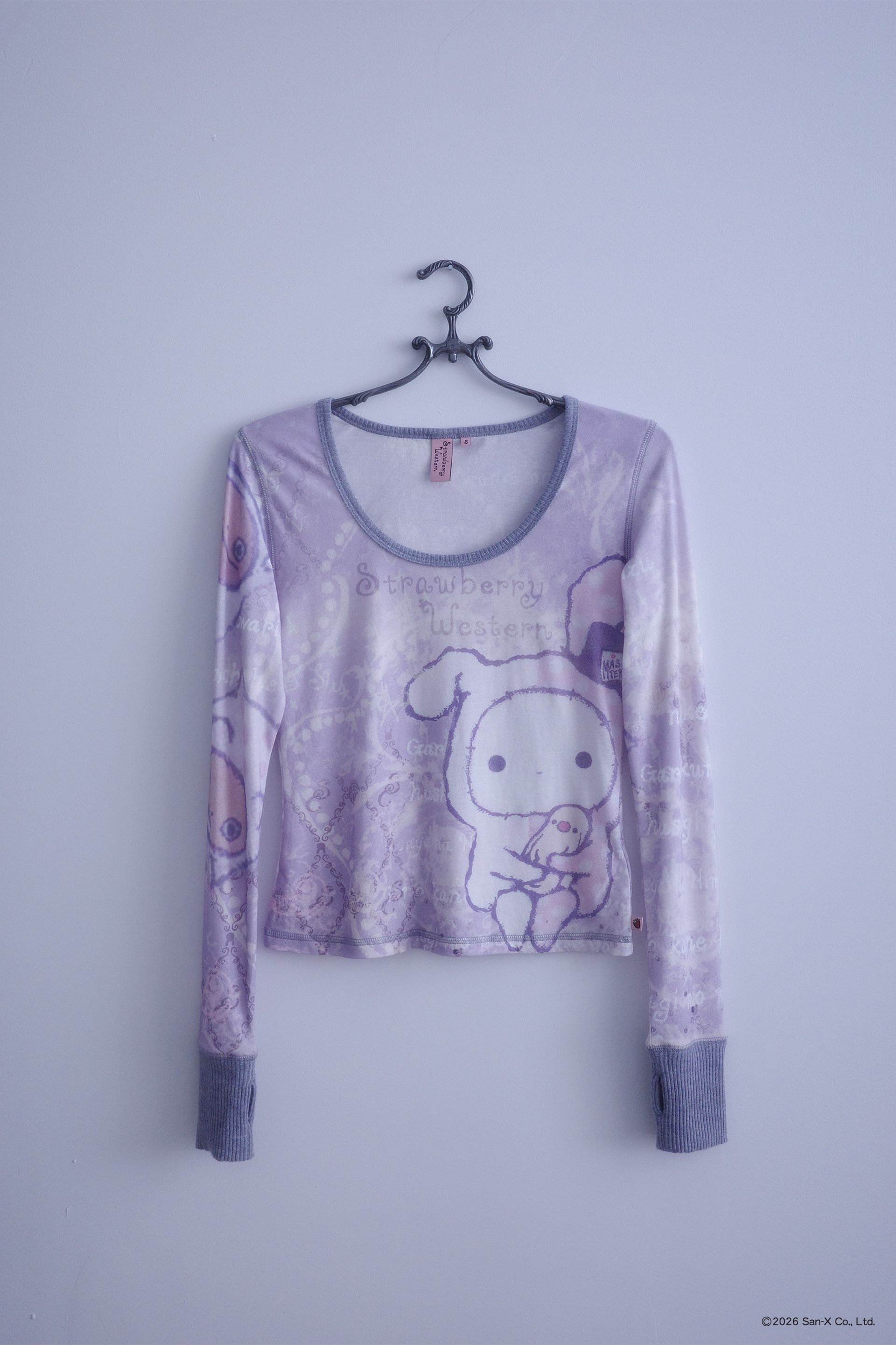 Flat image of a hanger holding An ethereal engineered print long-sleeve top featuring Shappo the Ringmaster. Cut from a lightweight, 110gsm 100% Cotton with chunky, heathered dusty purple ribbing at the neck and sleeve cuffs. The sleeves are finished with taller cuffs and built-in thumb holes, providing extra coverage and keeping your hands warm during the colder months.
