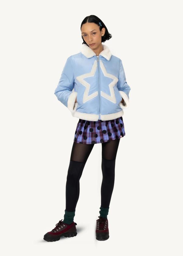 Model stands with hands in pockets of a baby blue puffer jacket with white faux fur collar, cuffs and star shape applique at front and a pleated skirt legging.