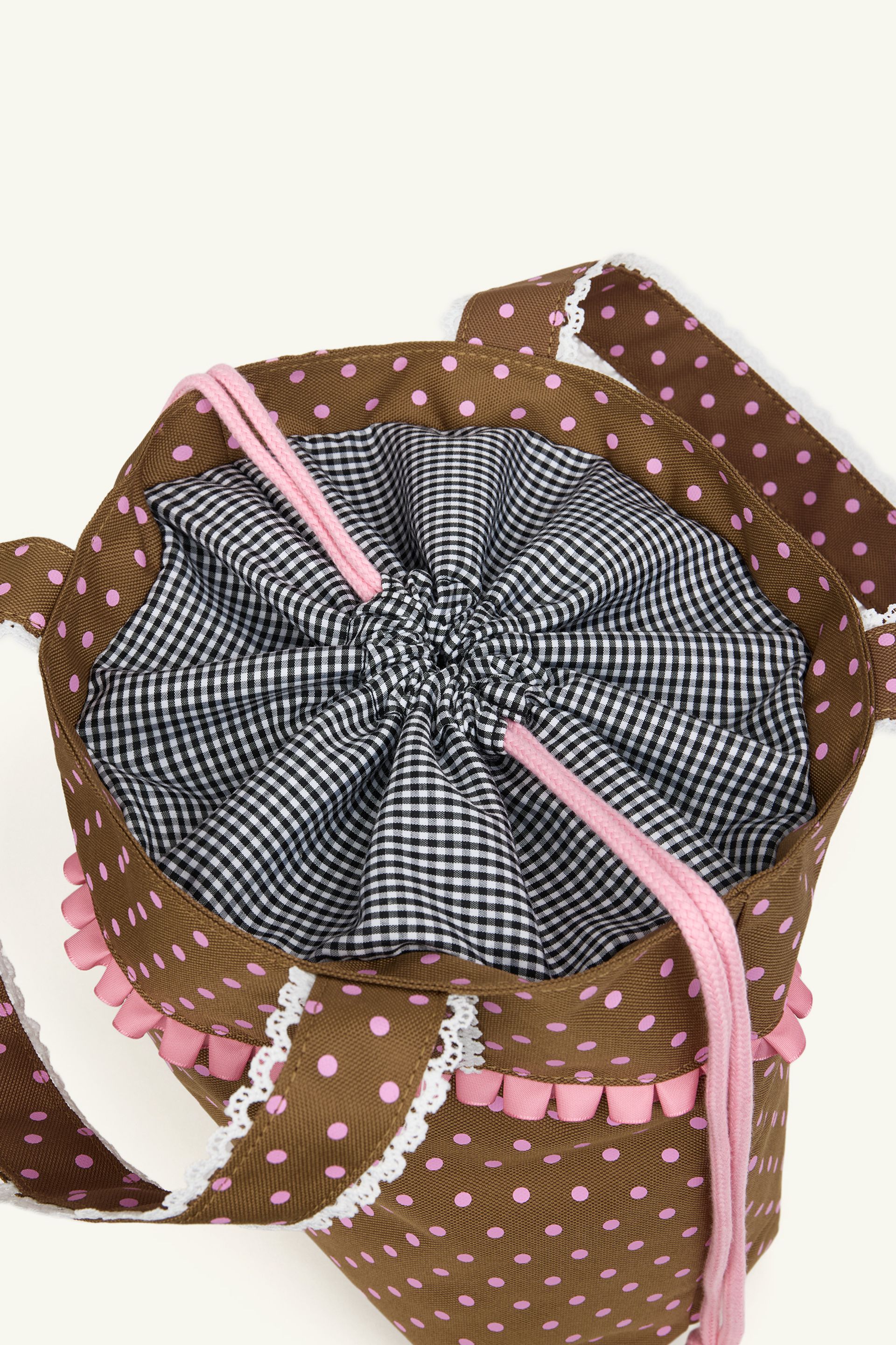 Detail view of the black and white gingham lining cinch closure on the olive green polka dot ruffle trim shoulder bag.