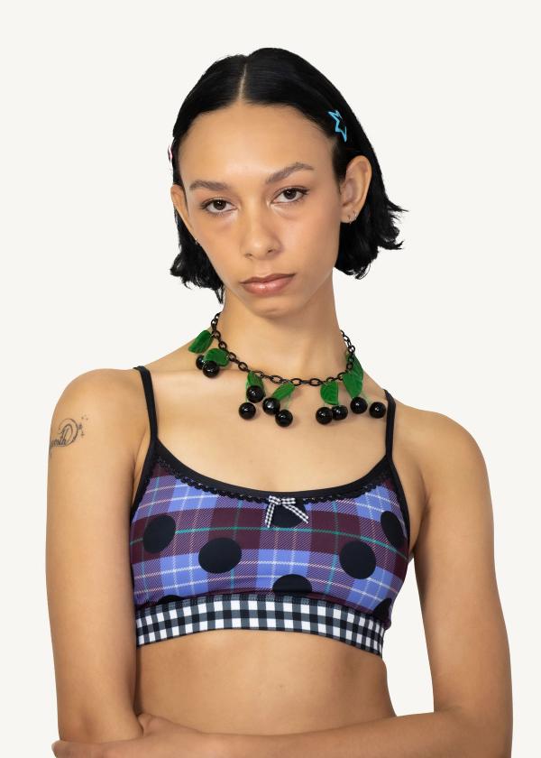 Closeup of model wearing plaid polka dot print sports bra with contrasting black and white gingham elastic band, picot elastic trimming and gingham ribbon at front. 