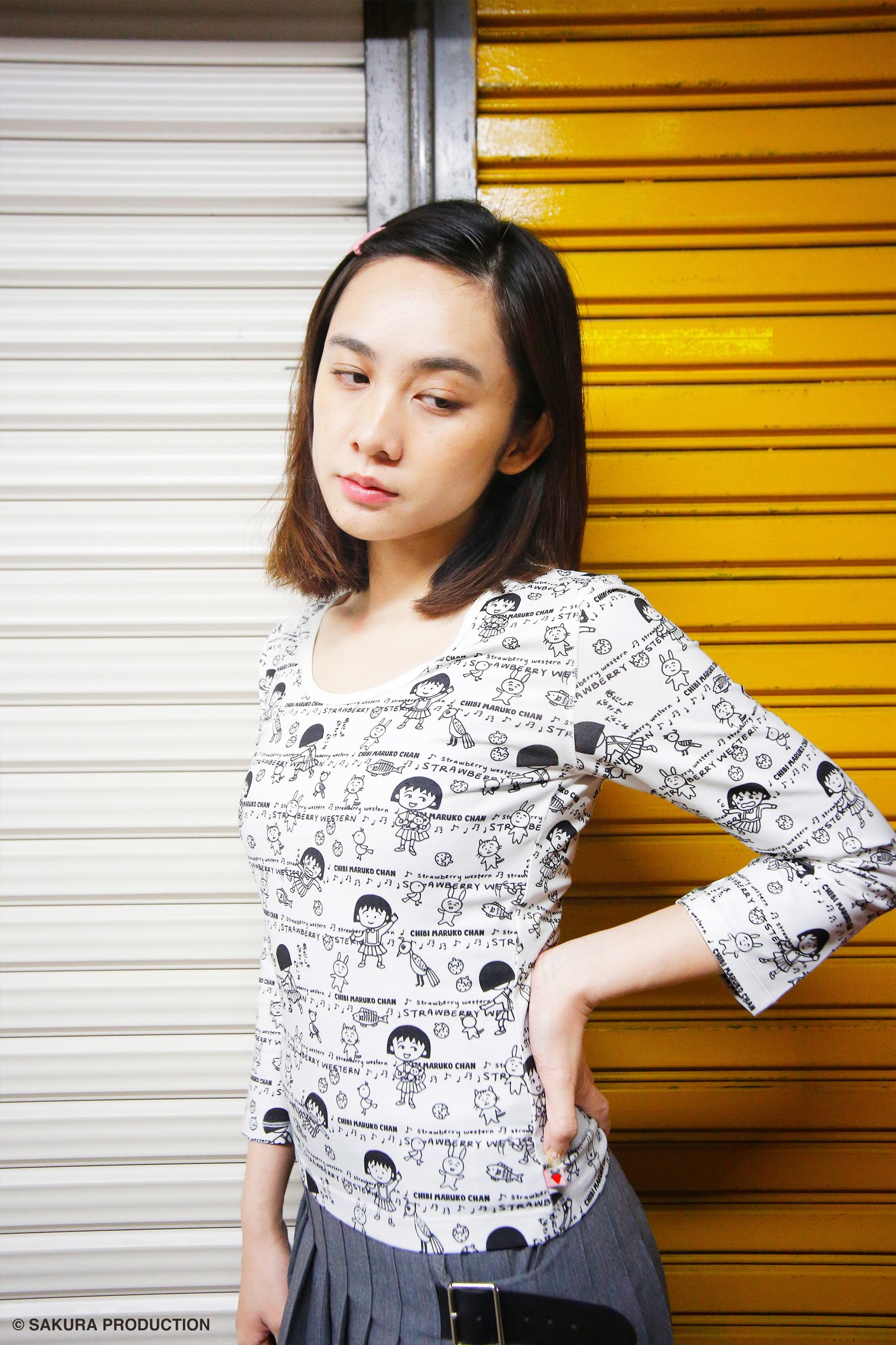 Girl standing against garage door wearing the Chibi Maruko Chan Playtime top. She puts her hand on her waist and looks down.