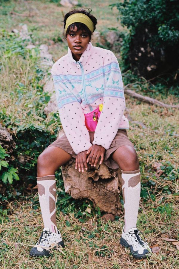 Woman sits on a tree stump wearing baby Pink fluffy jacquard knit sherpa jacket in a strawberry border motif with binding.