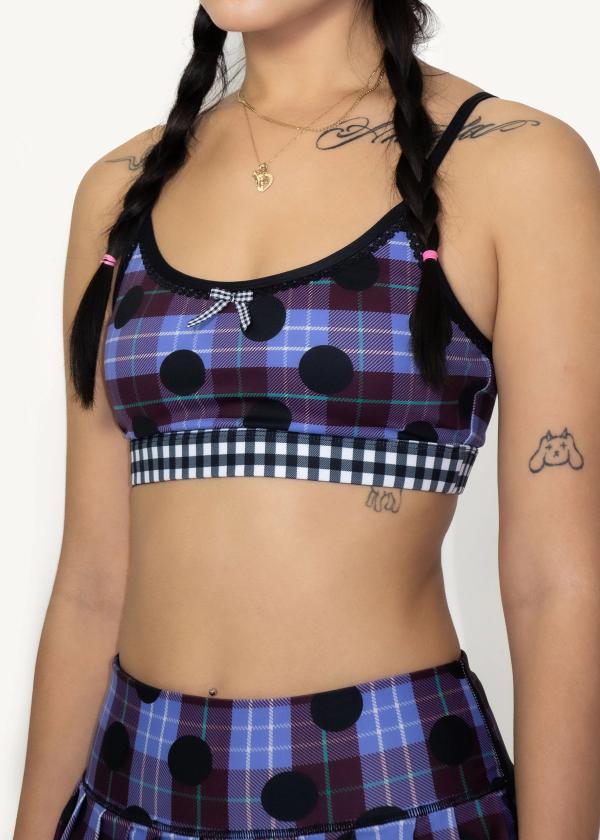 3/4 view closeup of model wearing plaid polka dot print sports bra with contrasting black and white gingham elastic band, picot elastic trimming and gingham ribbon at front. 