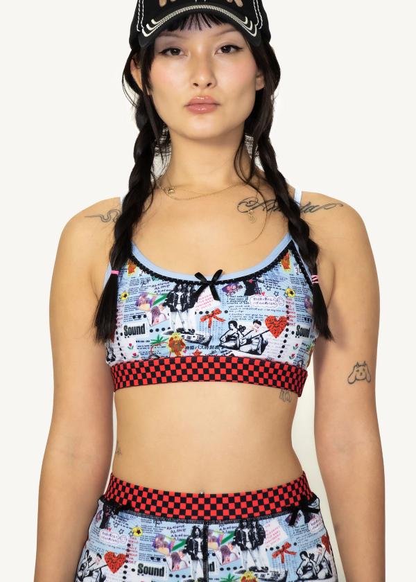 Closeup of model wearing sports bra in punk-style collage print with red and black checker waistband and a black bow.