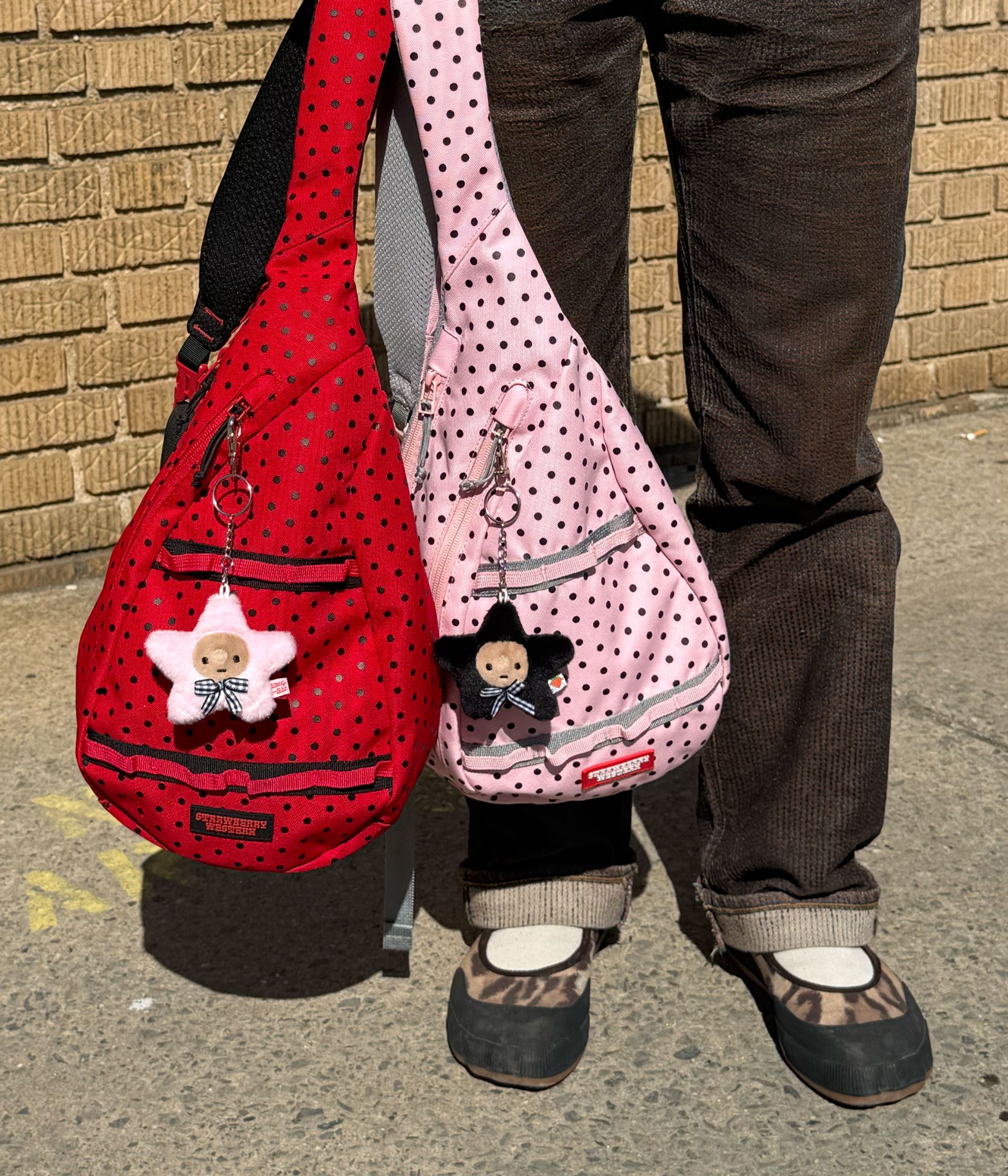 Close up of Red Sling Bag and Pink Sling bag being held in one hand outside on the street.
