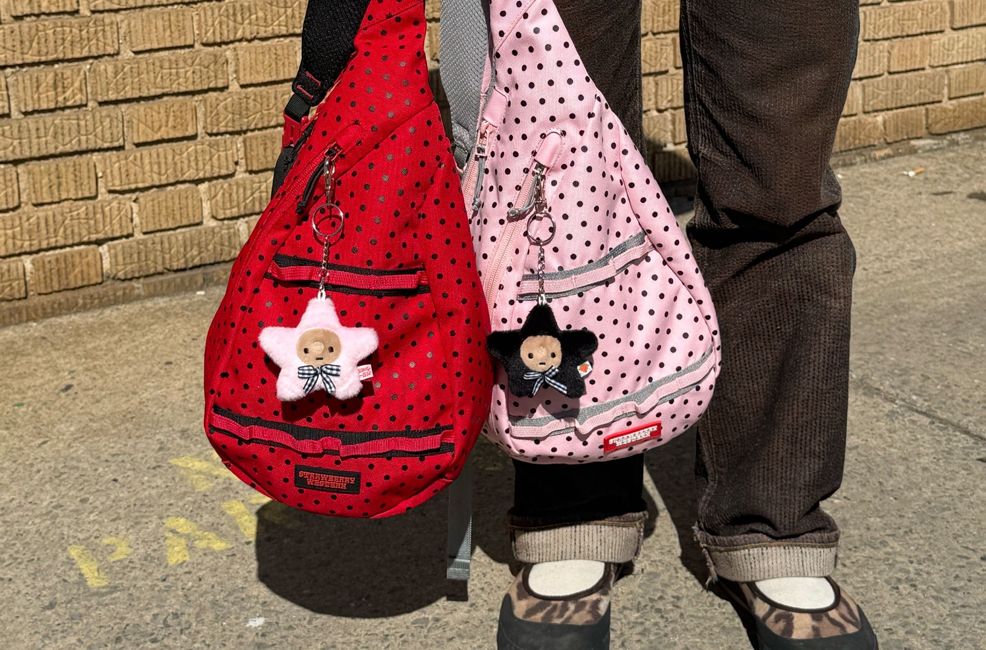 Close up of Red Sling Bag and Pink Sling bag being held in one hand outside on the street.