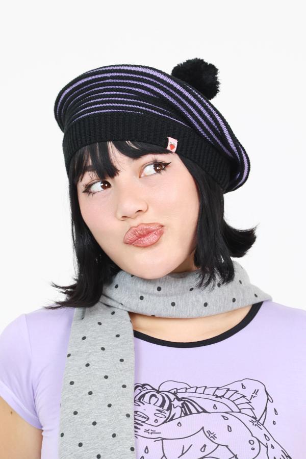 Model wearing lavender and black dimensional striped knit beret beanie with decorative pompom. 