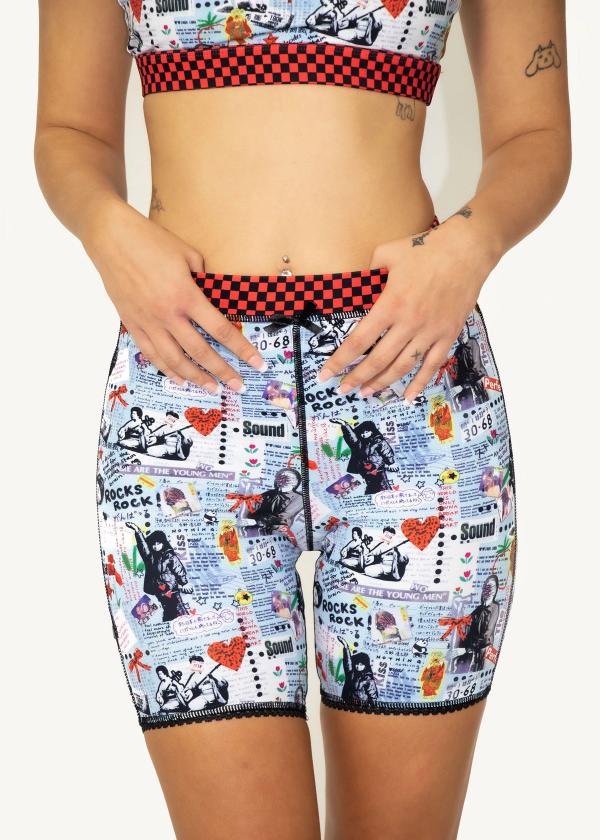 Close up of woman's body wearing bike shorts in a punk-style collage print with red and black checker waistband.