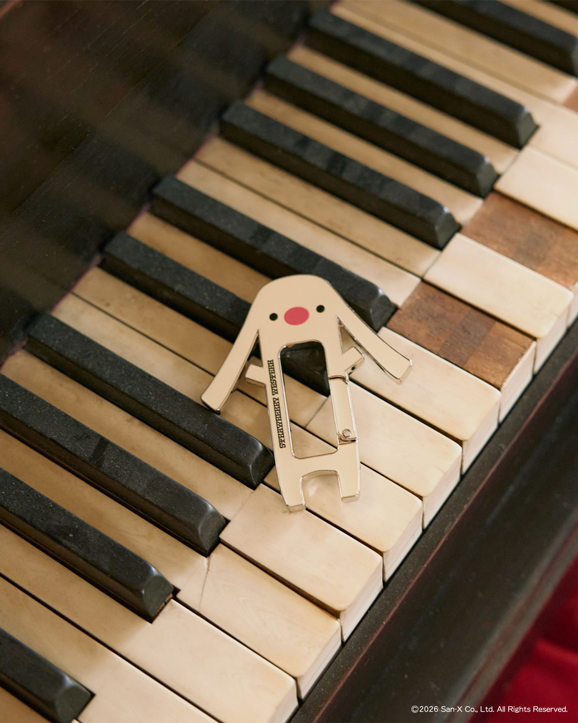 Toto, a character from Sentimental Circus, Carabiner Keychain laid out on the broken keys of a grand piano.