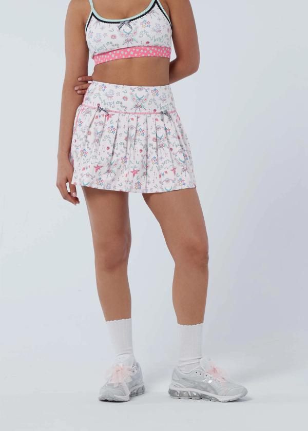 Half body view of woman wearing a pleated workout skort in a fairy-like starbaby print with pink stitching and two black and white gingham bows at front waist and a matching sports bra.