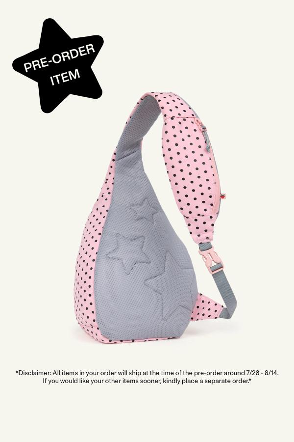 Product image of back view of a Pink sling backpack with black polka dots and a gray padded panel featuring embossed star shapes. The bag has a gray adjustable strap with a pink buckle and a small zip pocket on the strap. In the top left corner, a black star reads "Pre-Order Item." Bottom reads “Disclaimer: All items in your order will ship at the time of the pre-order around 7/26-8/14. If you would like your other items sooner, kindly place a separate order.