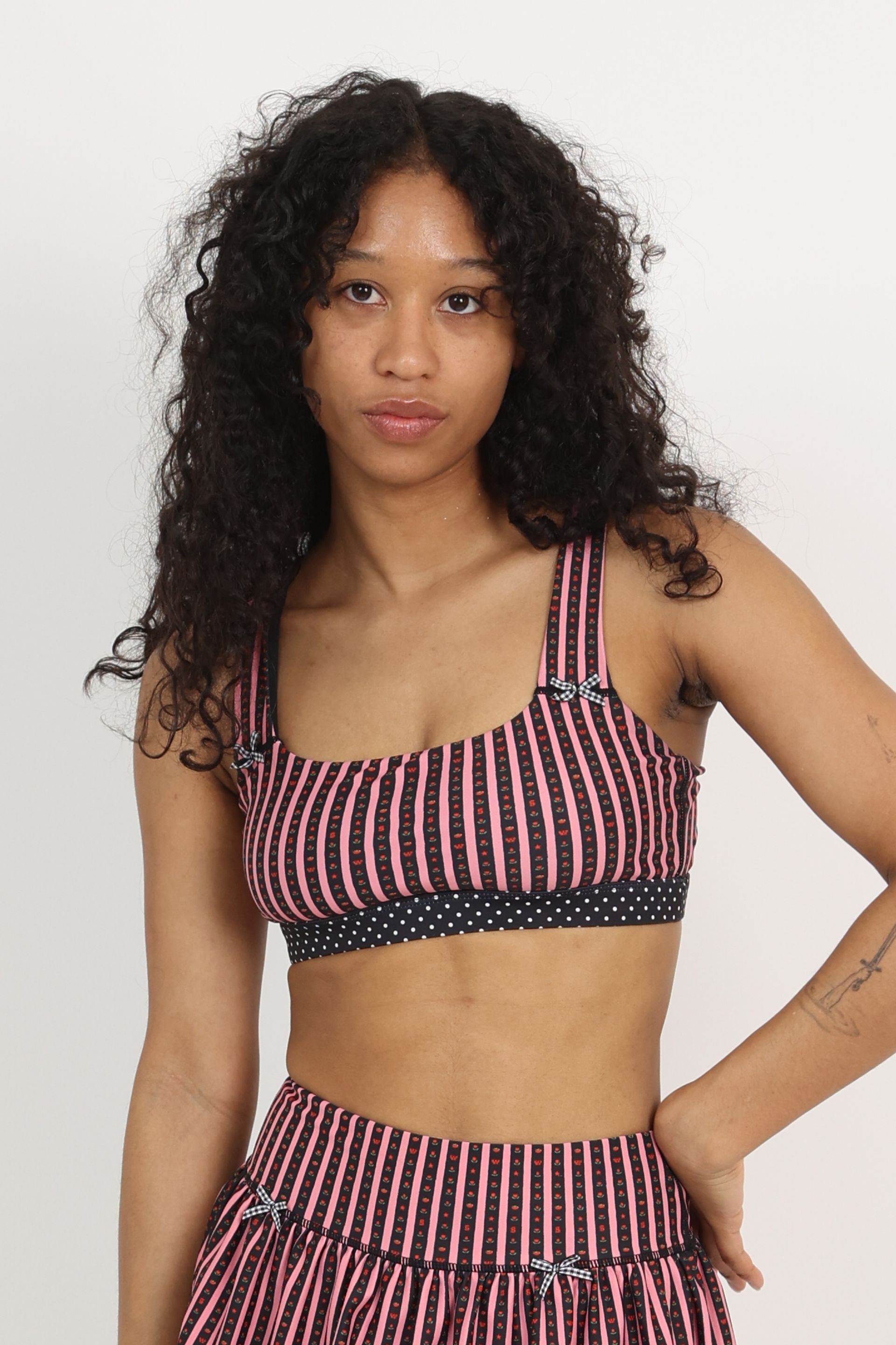 Front view of medium-support Coco Sports Bra silhouette featuring a hand-drawn, floral border stripe print in Pink/Black with contrast polka dot print elastic band and gingham bow details.