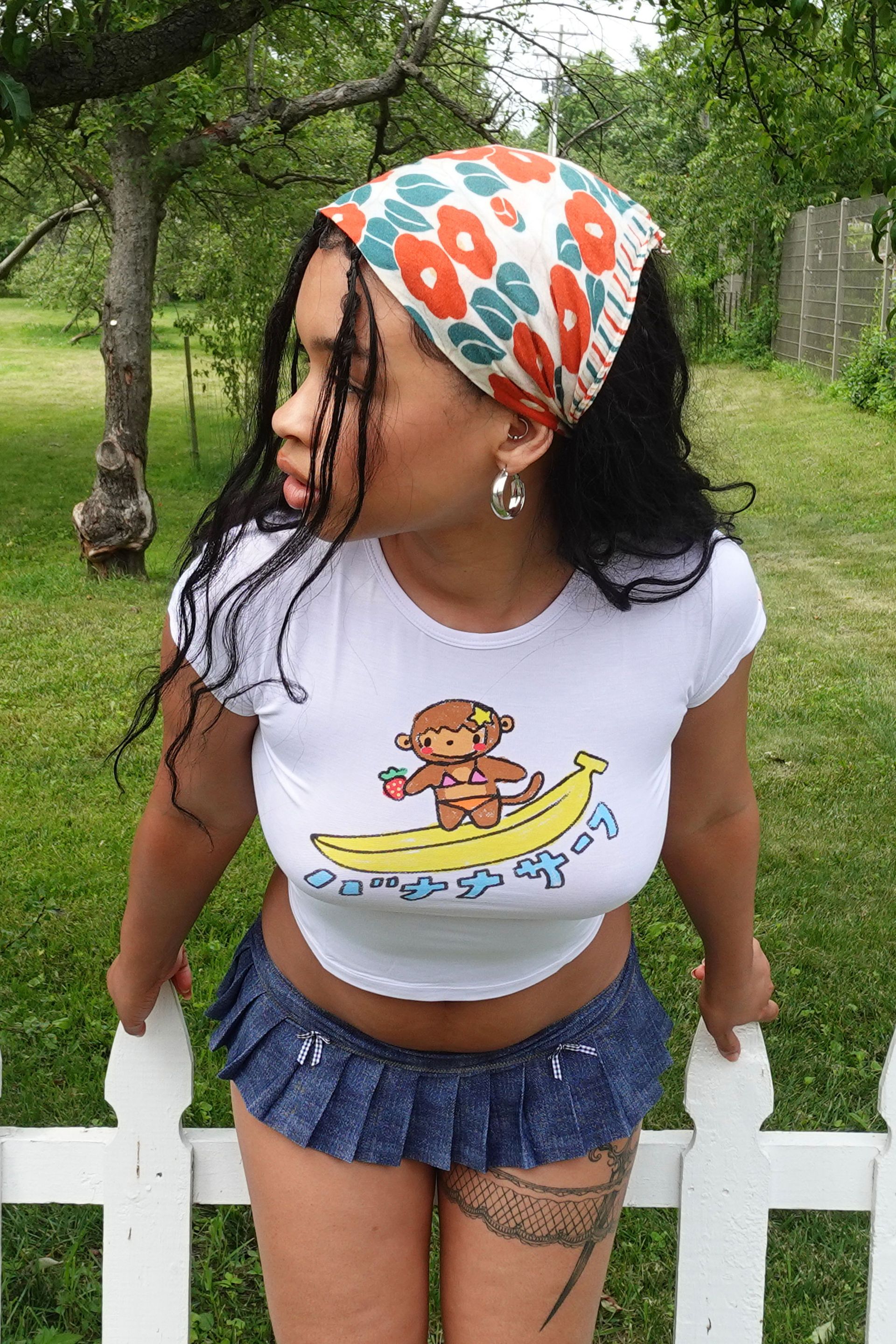 White slim fit baby tee with a hand-drawn surfing monkey graphic that says 'Banana Surf' in Japanese below it.