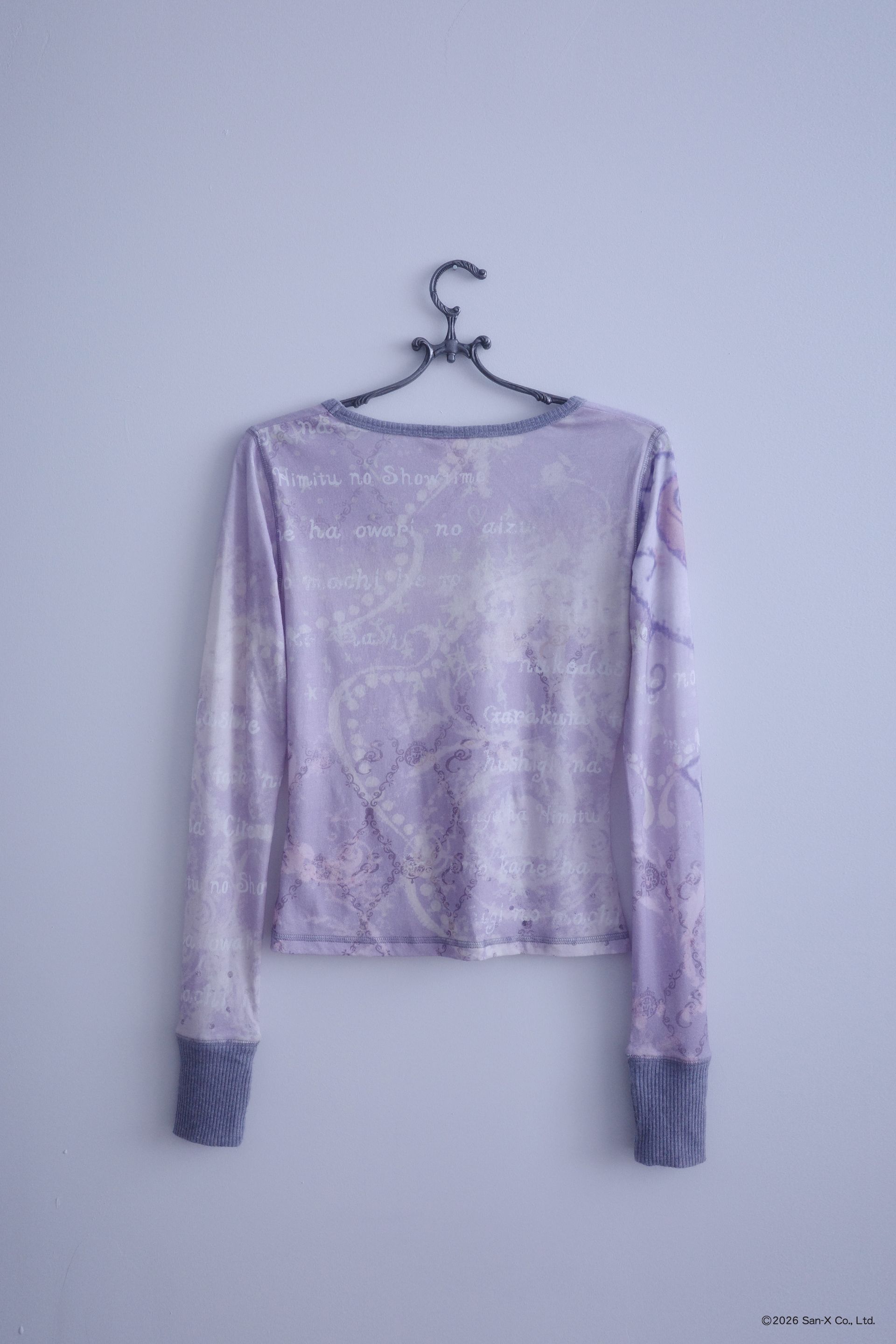 Flat image of a hanger holding an ethereal engineered print long-sleeve top featuring Shappo the Ringmaster. Cut from a lightweight, 110gsm 100% Cotton with chunky, heathered dusty purple ribbing at the neck and sleeve cuffs. The sleeves are finished with taller cuffs and built-in thumb holes, providing extra coverage and keeping your hands warm during the colder months.