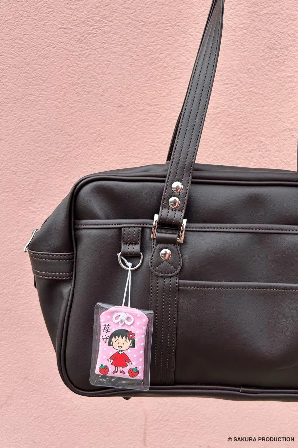 Chibi Maruko Chan omamori hanging off a messenger bag posed against a pink wall.