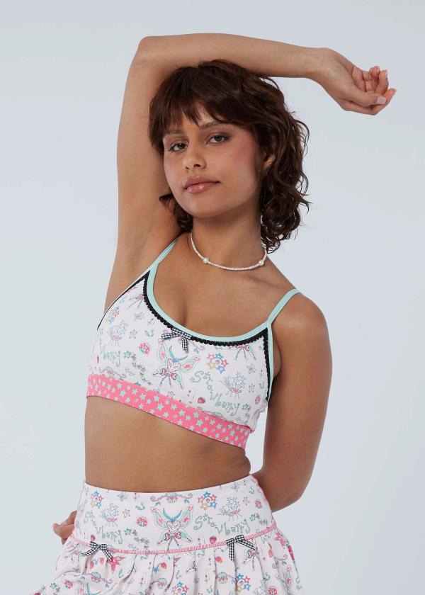 Woman with one arm bent above her head and one  bent behind her back wearing a bralette silhouette sports bra in a fairy-like starbaby print with a pink and mint green shooting star waistband, black picot trimming, mint binding and a black and white gingham bow at front.